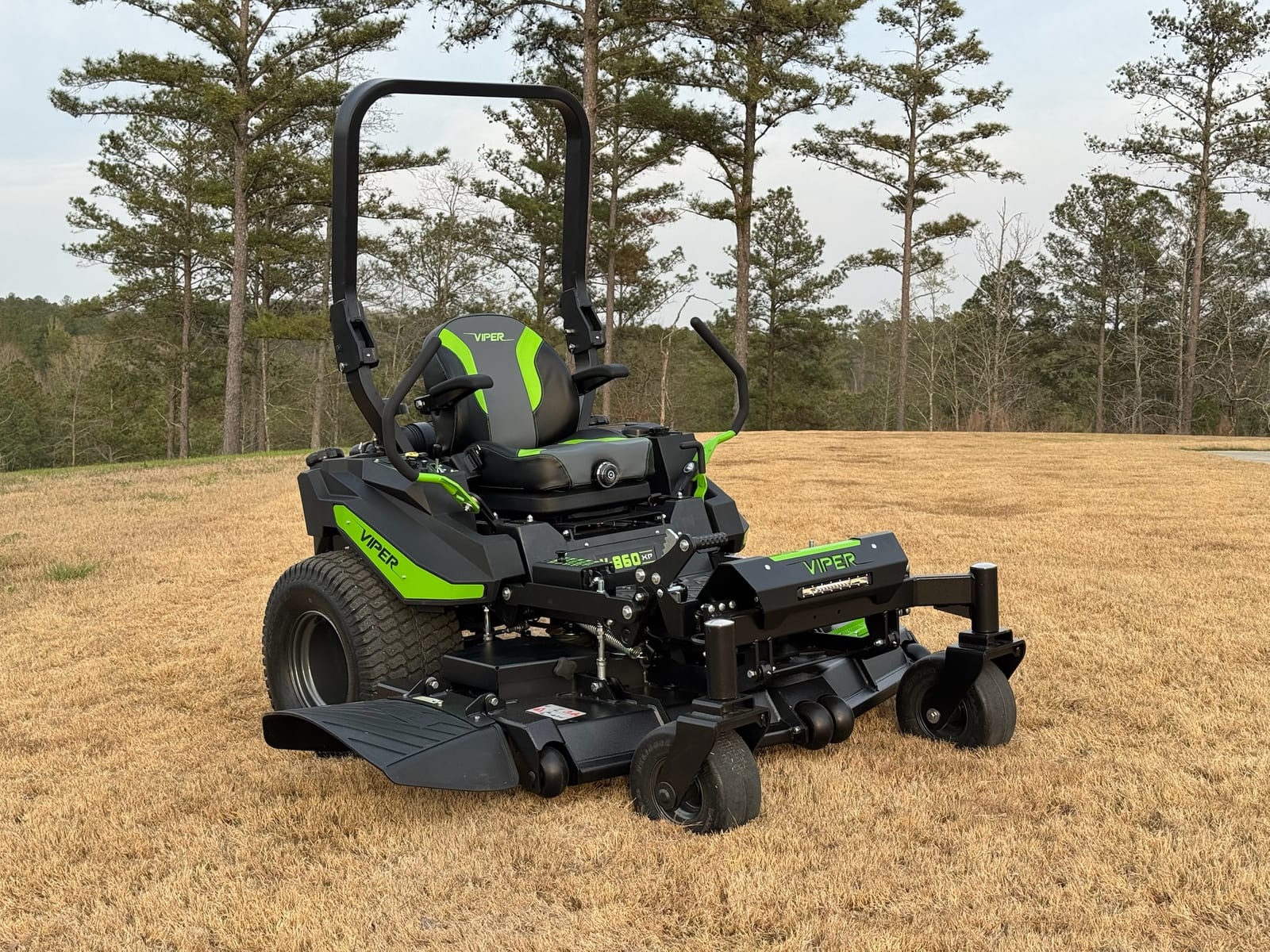 A commercial zero-turn mower on a green lawn with a pine treeline behind