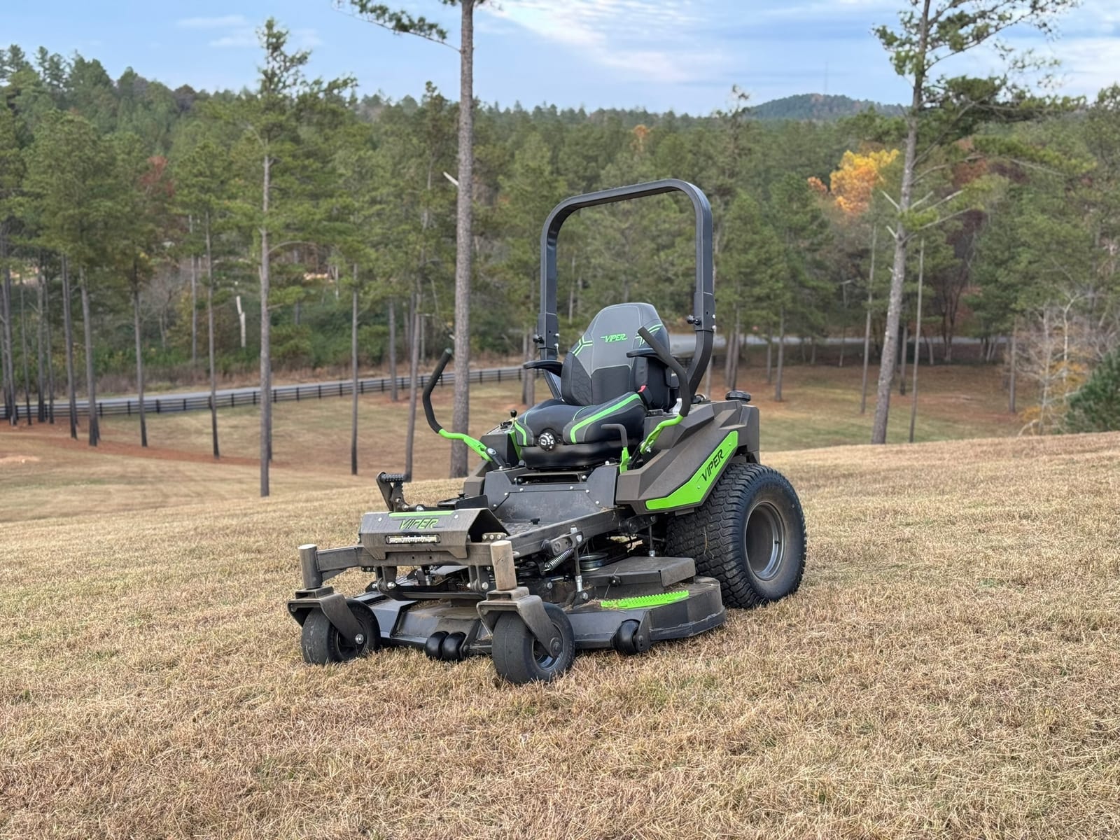 A commercial zero-turn mower on a wide open field with a pine treeline