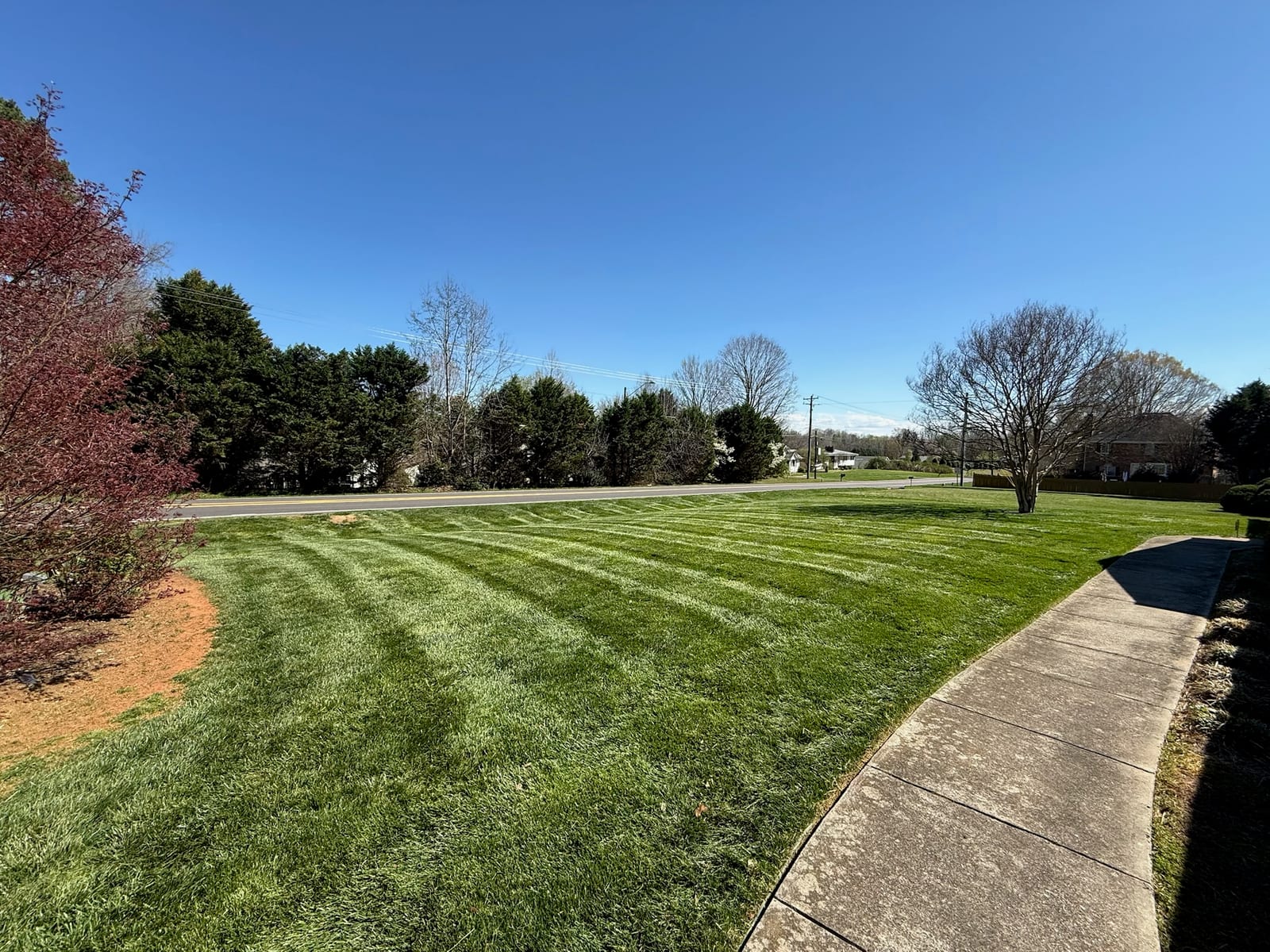 A green, striped lawn along a residential sidewalk