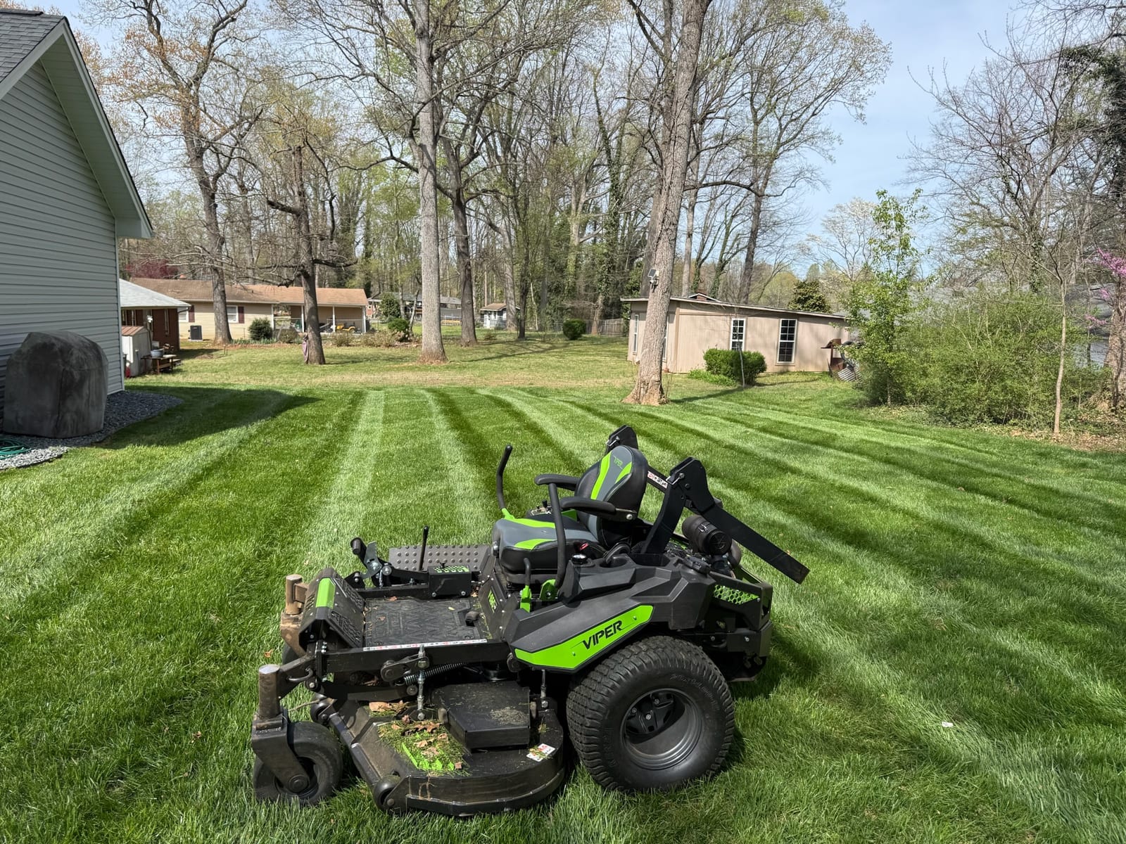 A zero-turn mower on a green, freshly striped residential lawn