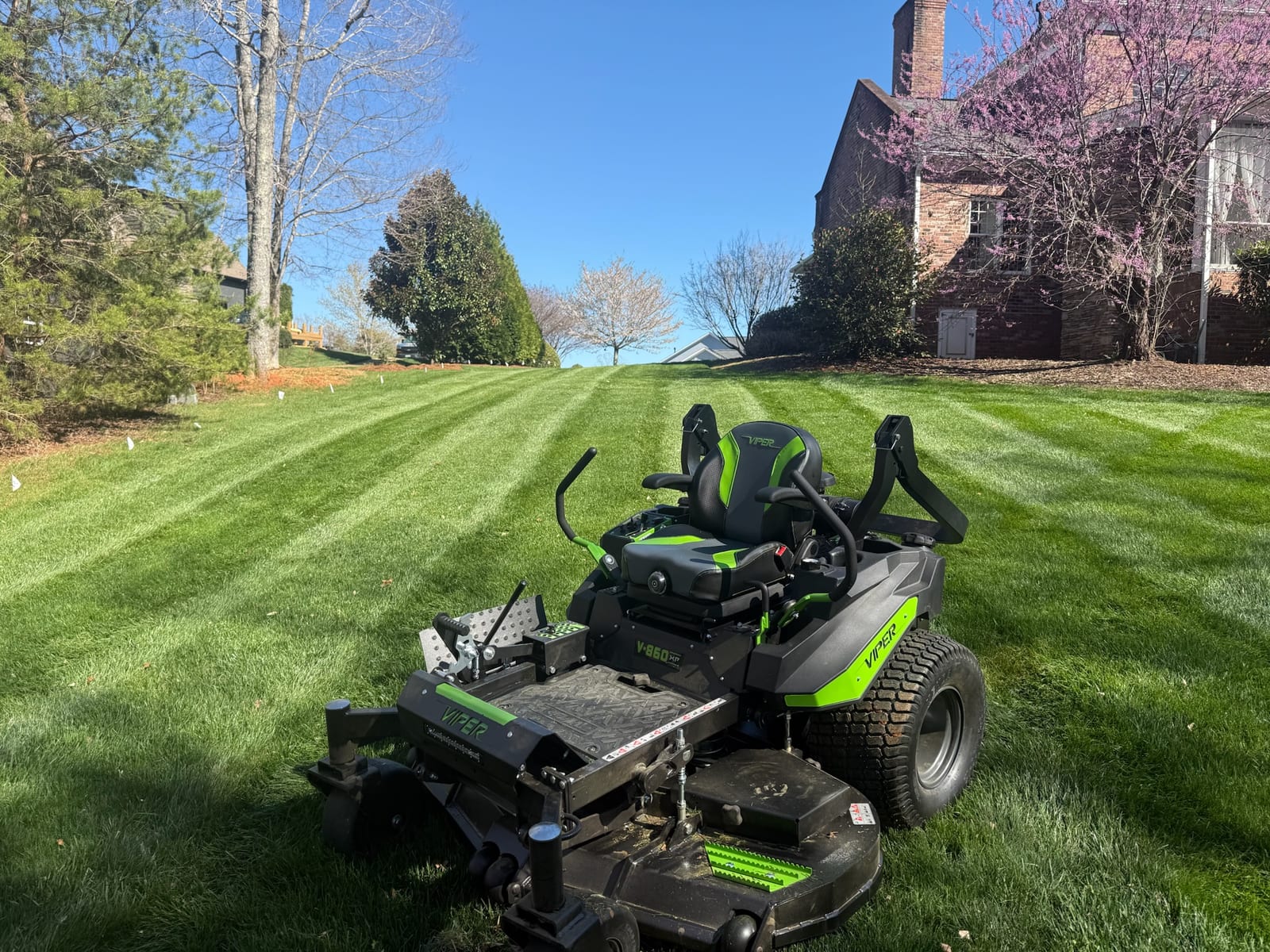 A zero-turn mower on a freshly striped spring lawn in front of a brick home